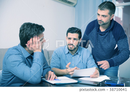 Three troubled men discussing documents at desk 38710041