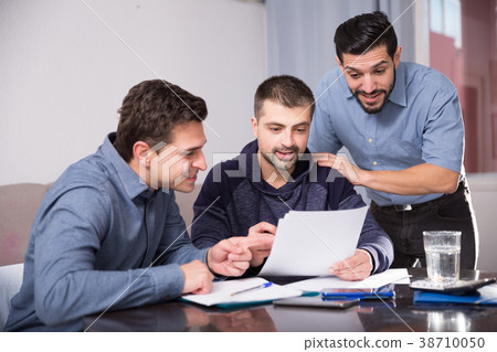 Two positive men helping friend with documents at table 38710050