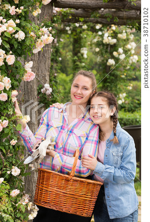 female with long curly hair and girl standing near roses flower outdoors female with long curly hair and girl standing near roses flower outdoors 38710102