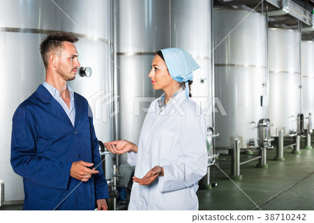 Two workers in protective uniform talking in secondary fermentation section Two workers in protective uniform talking in secondary fermentation section 38710242