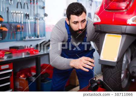 Male worker fixing failed scooter in workshop Male worker fixing failed scooter in workshop 38711066