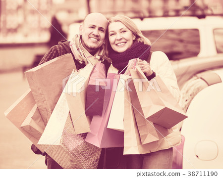 elderly couple carrying purchases and smiling outdoors elderly couple carrying purchases and smiling outdoors 38711190
