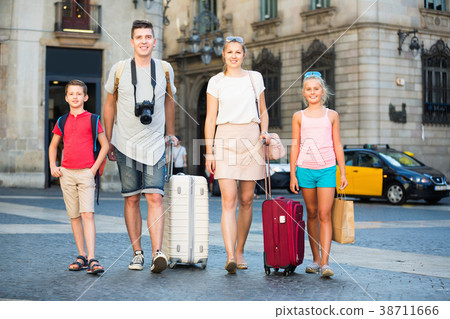 Traveling family of four strolling with luggage along European city street 38711666
