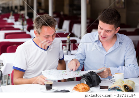 two friendly men sitting with coffee and looking at map in cafe two friendly men sitting with coffee and looking at map in cafe 38712184