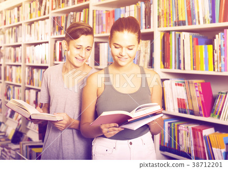 portrait of teenage boy and girl customers looking at open book standing among bookshelves portrait of teenage boy and girl customers looking at open book standing among bookshelves 38712201