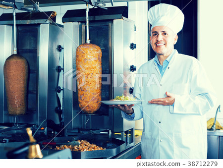 man chef wearing uniform cutting meat for kebab on kitchen in fa man chef wearing uniform cutting meat for kebab on kitchen in fa 38712279