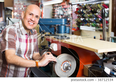 Workman resharpening knives on machine. Workman resharpening knives on machine. 38712534