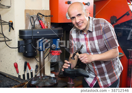 Workman repairing pair of shoes . 38712546