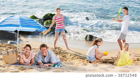Couple relaxing on beach while their kids playing active games 38712548