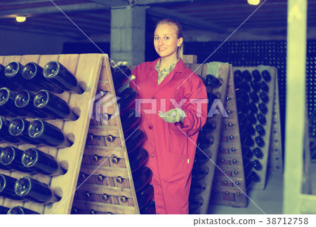 Woman in uniform working with bottle storage racks in winery cellar Woman in uniform working with bottle storage racks in winery cellar 38712758