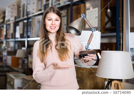 Portrait of cheerful woman buyer choosing modern lamp in furniture shop 38714090