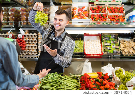 male shopping assistant helping customer to buy fruit and vegetables in grocery shop male shopping assistant helping customer to buy fruit and vegetables in grocery shop 38714094