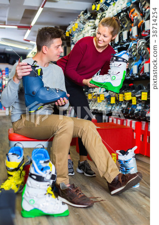Saleswoman is helping man to trying on boots for skiing Saleswoman is helping man to trying on boots for skiing 38714254