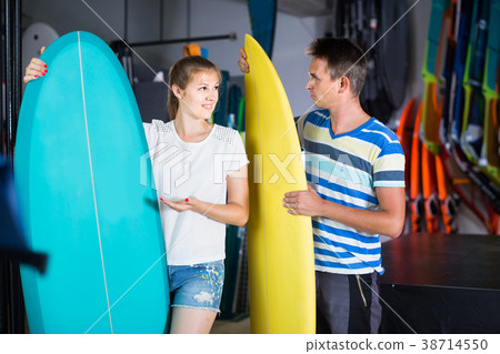 couple is demonstraiting surfboard in nautical shop. 38714550