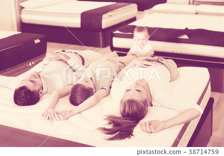 Young cheerful family lying on back on white mattress, testing quality Young cheerful family lying on back on white mattress, testing quality 38714759