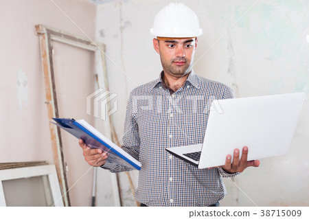 Portrait of serious architect working at the notebook in helmet with documents Portrait of serious architect working at the notebook in helmet with documents 38715009