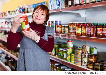 female buyer choosing canned jar of tomato paste at the supermarket 38715115
