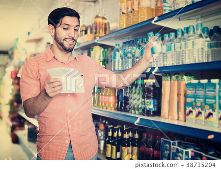 Man is choosing water with help note list in supermarket. 38715204