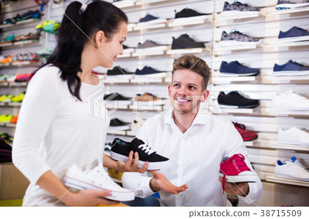 Smiling seller demonstrating sneakers to female 38715509