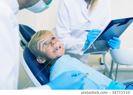 Male dentist with female assistant are diagnosticating to young patient which is sitting 38715510