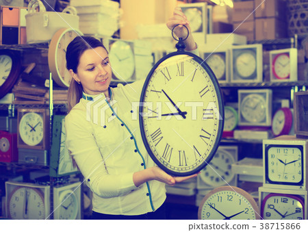 Woman is choosing new clock for her home in the store. Woman is choosing new clock for her home in the store. 38715866