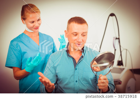 Patient is analysing his skin with using mirror after the procedure 38715918