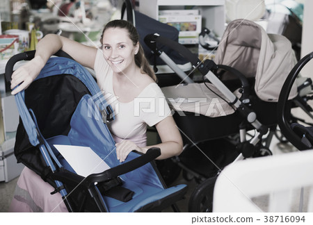 smiling pregnant woman looking for baby carriage at kids shop smiling pregnant woman looking for baby carriage at kids shop 38716094