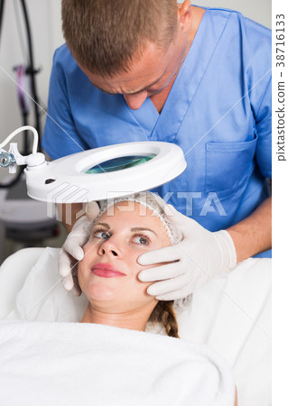 Specialist is analysing skin of female patient with using magnification before the procedure 38716133