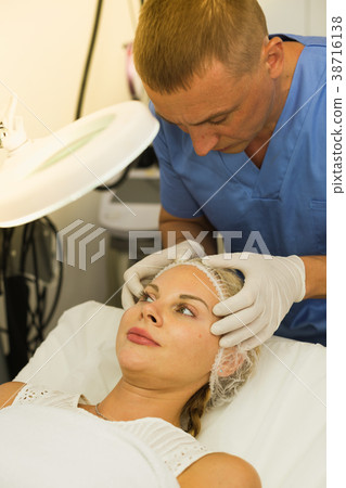 Specialist is analysing skin of female patient with using magnification before the procedure 38716138