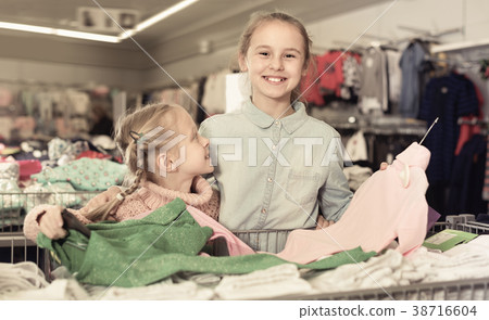 Two small happy sisters satisfied with purchases in children clo 38716604