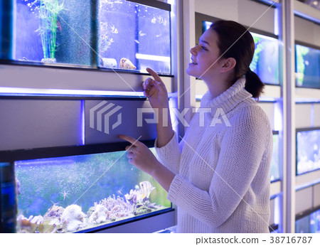 Girl in aquarium shop is looking at different colored fish 38716787