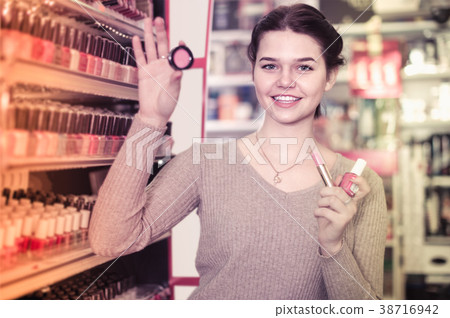 Smiling woman customer deciding on make-up items in cosmetics shop Smiling woman customer deciding on make-up items in cosmetics shop 38716942