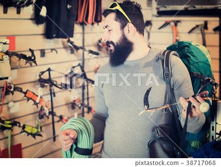 concentrated male customer examining climbing equipment in sports equipment store 38717068