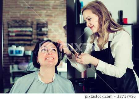 Young haircut master is doing hairstyle and cut by means of scissors 38717456