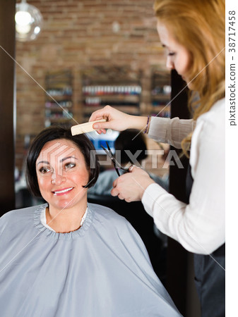 Hairdresser does to woman haircut with use of scissors and hairbrushes 38717458