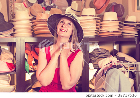 adult smiling woman try on boater hat in shopping mall 38717536