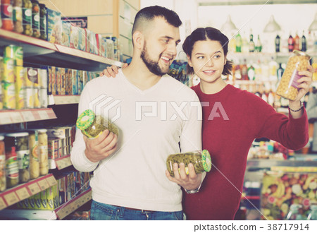 Couple standing near shelves with canned goods at store Couple standing near shelves with canned goods at store 38717914