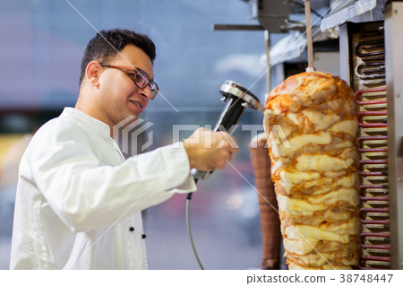 chef slicing doner meat from spit at kebab shop 38748447