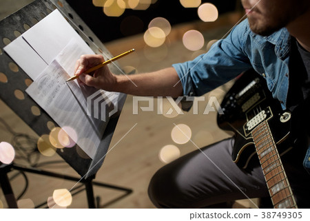 man with guitar writing to music book at studio 38749305