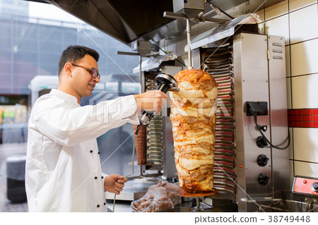 chef slicing doner meat from spit at kebab shop 38749448