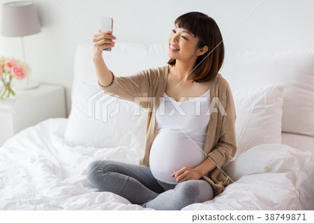 pregnant woman taking selfie by smartphone at home pregnant woman taking selfie by smartphone at home 38749871