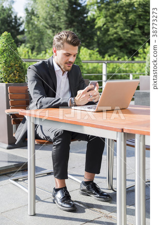 Man in black suit and looking into smart phone Man in black suit and looking into smart phone 38773273