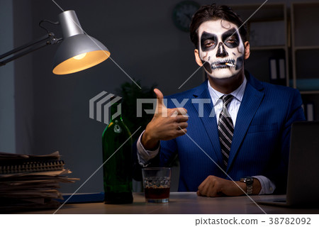 Businessman with scary face mask working late in Businessman with scary face mask working late in 38782092