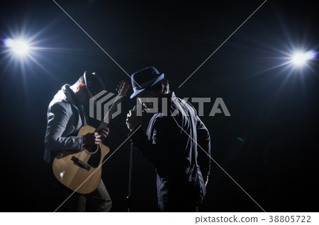 Musician Duo band hand holding the microphone and singing a song and playing the guitar on black background with spot light and lens flare, musical concept Musician Duo band hand holding the microphone and singing a song and playing the guitar on black background with spot light and lens flare, musical concept 38805722