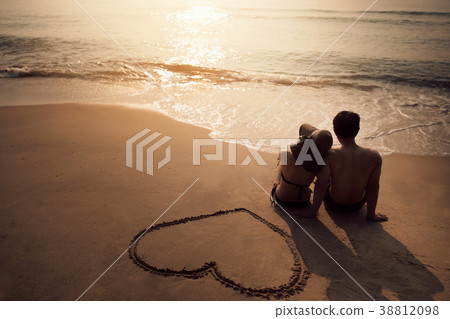 Couple sitting at the beach He was drawing a heart 38812098