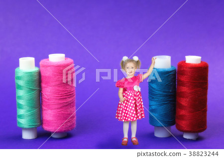 The girl is 3 years standing next to the huge coils of thread on a blue background. The girl is 3 years standing next to the huge coils of thread on a blue background. 38823244