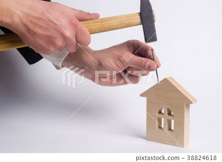 Man hammers a nail in a miniature wooden house Man hammers a nail in a miniature wooden house 38824618