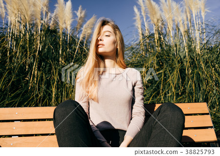 girl sits on a bench outdoors in the sun, warm 38825793