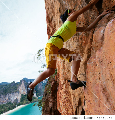 female rock climber climbing on seaside cliff 38839268