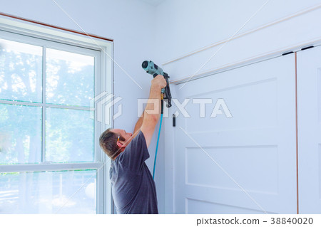 Carpenter using nail gun to moldings on doors 38840020